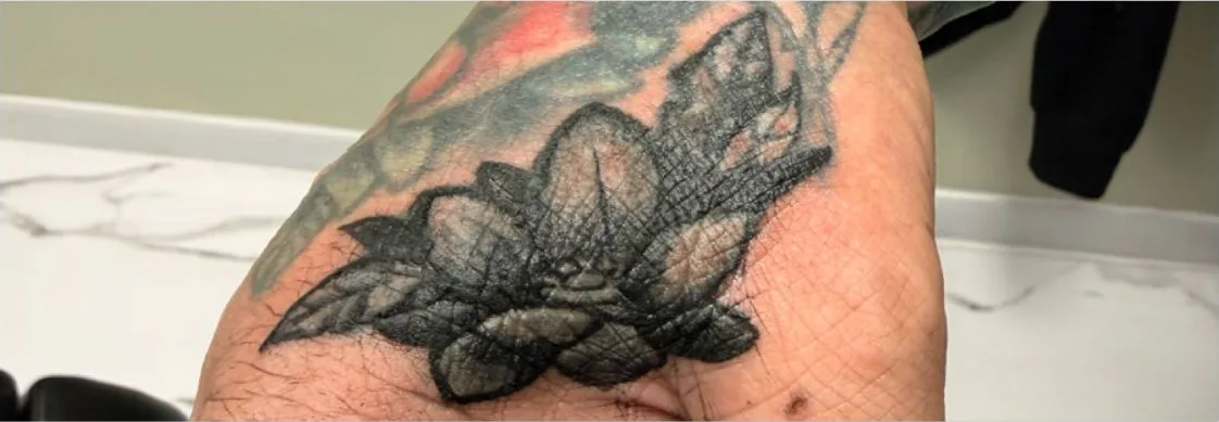 Finished black and grey lily cover-up on the hand, covering an old name tattoo