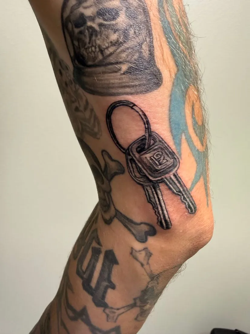 Black and grey realism keys tattoo beneath a skull on the leg