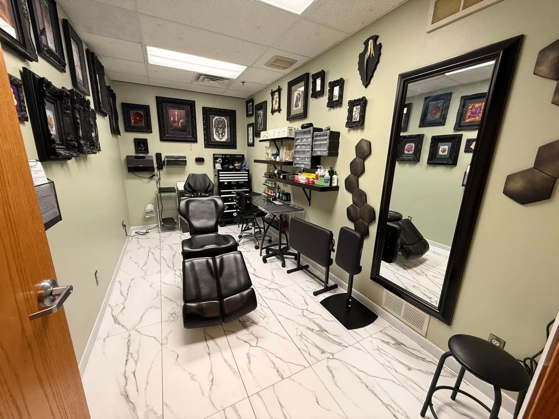 Inside The Ivory Needle: a black tattoo chair, framed artwork on the walls and marble floors